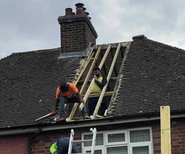 This is a photo of a roof repair being carried out. A section of the roof has been stripped and two roofers are replacing the rafters. Works being carried out by CGT Roofing Newport Pagnell